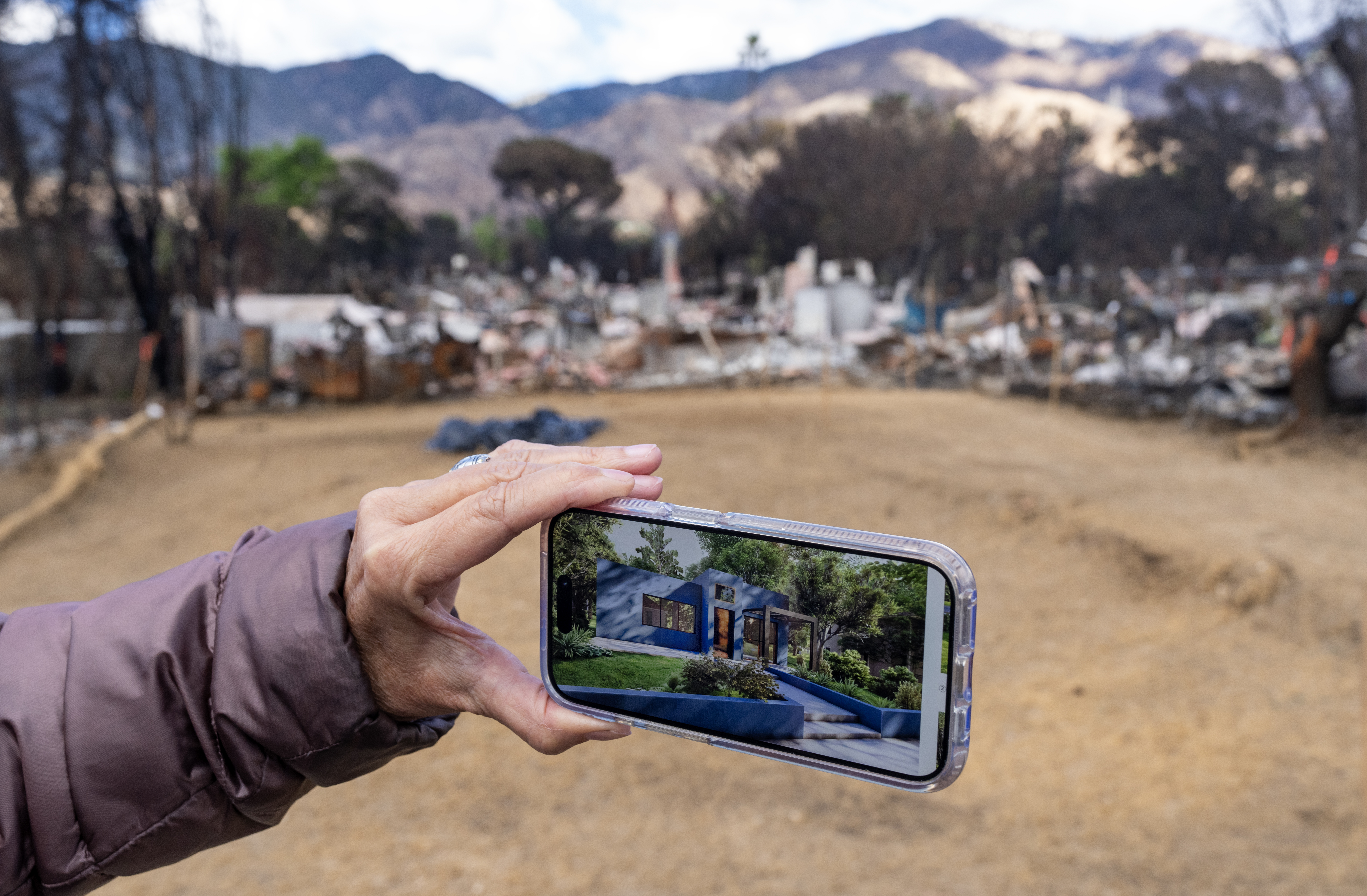 Hand of a person holding a cellphone with a model of a home in front of an empty land